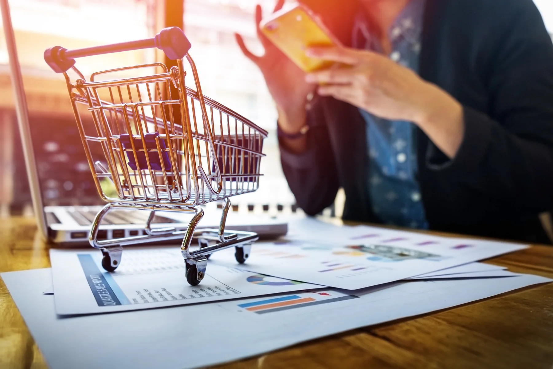 Carrito de compras junto a una persona realizando una compra digital